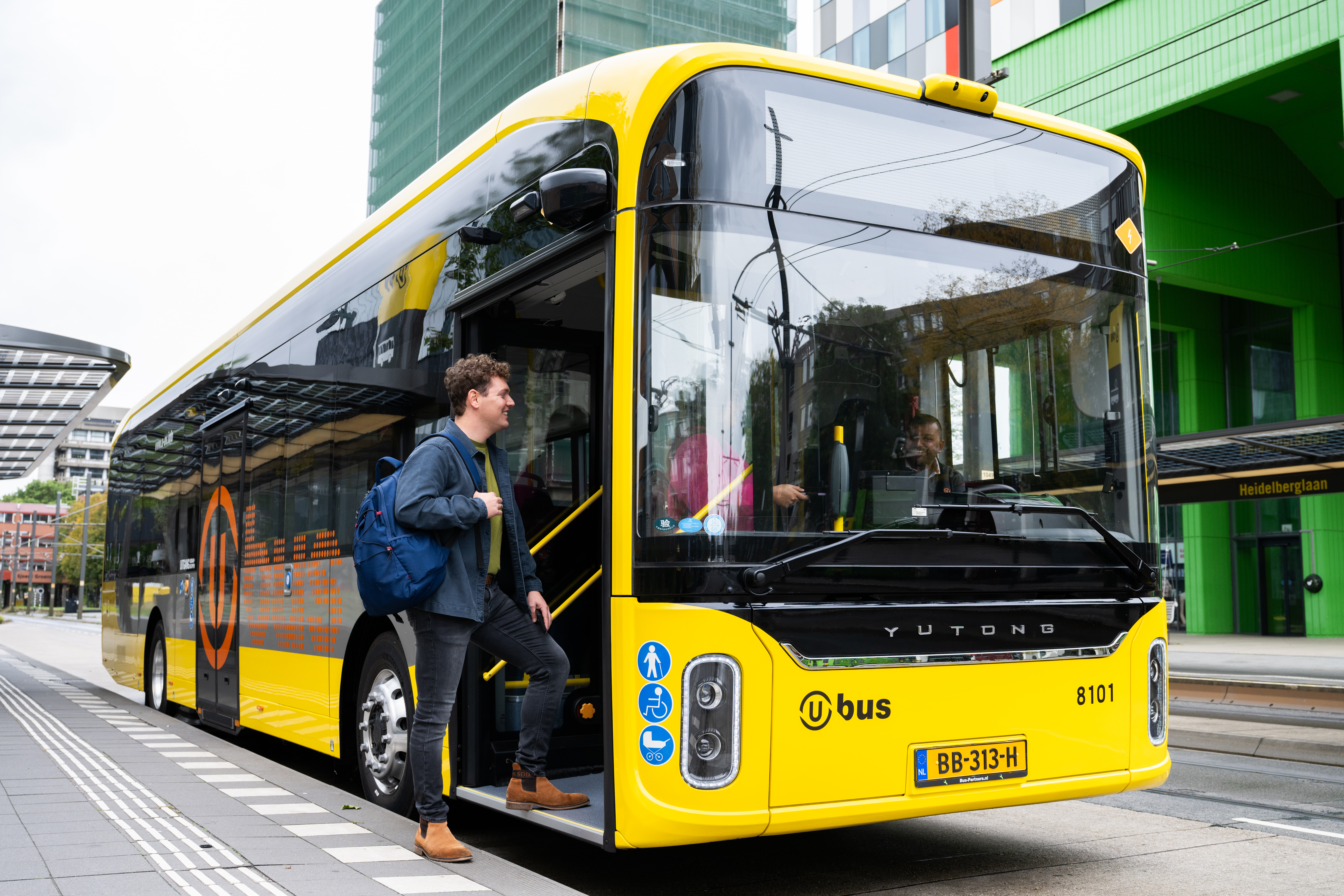 Reiziger met een rugzak stapt in in een gele UOV bus.