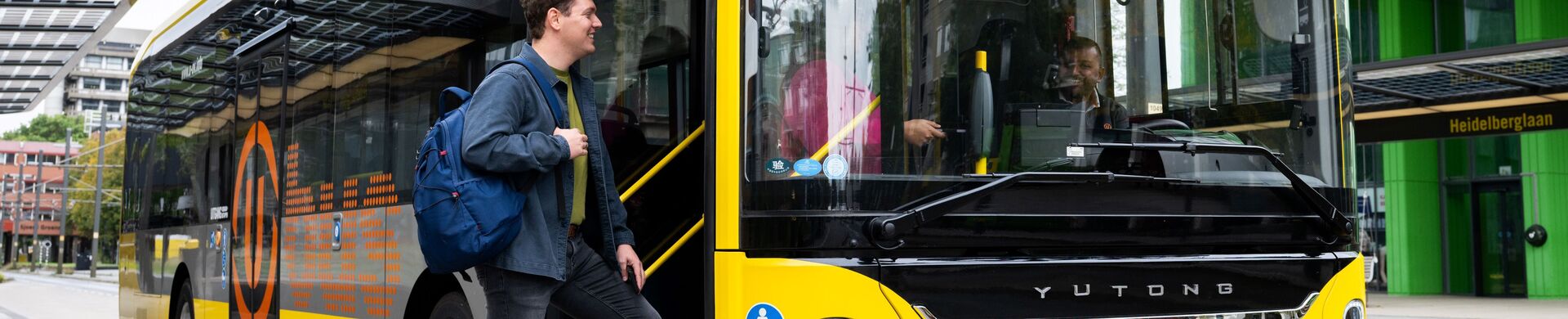Traveler with a backpack boards a yellow U-OV bus