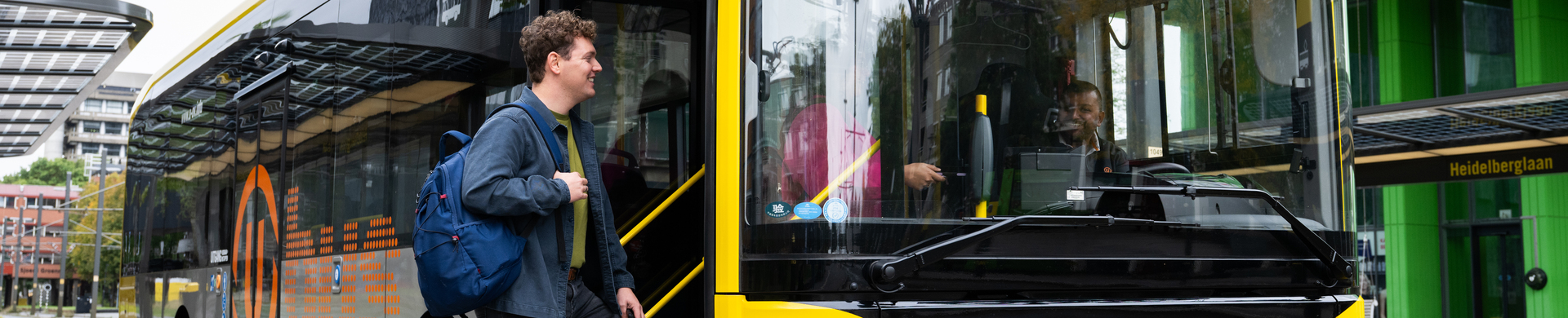 Reiziger met een rugzak stapt in in een gele UOV bus.