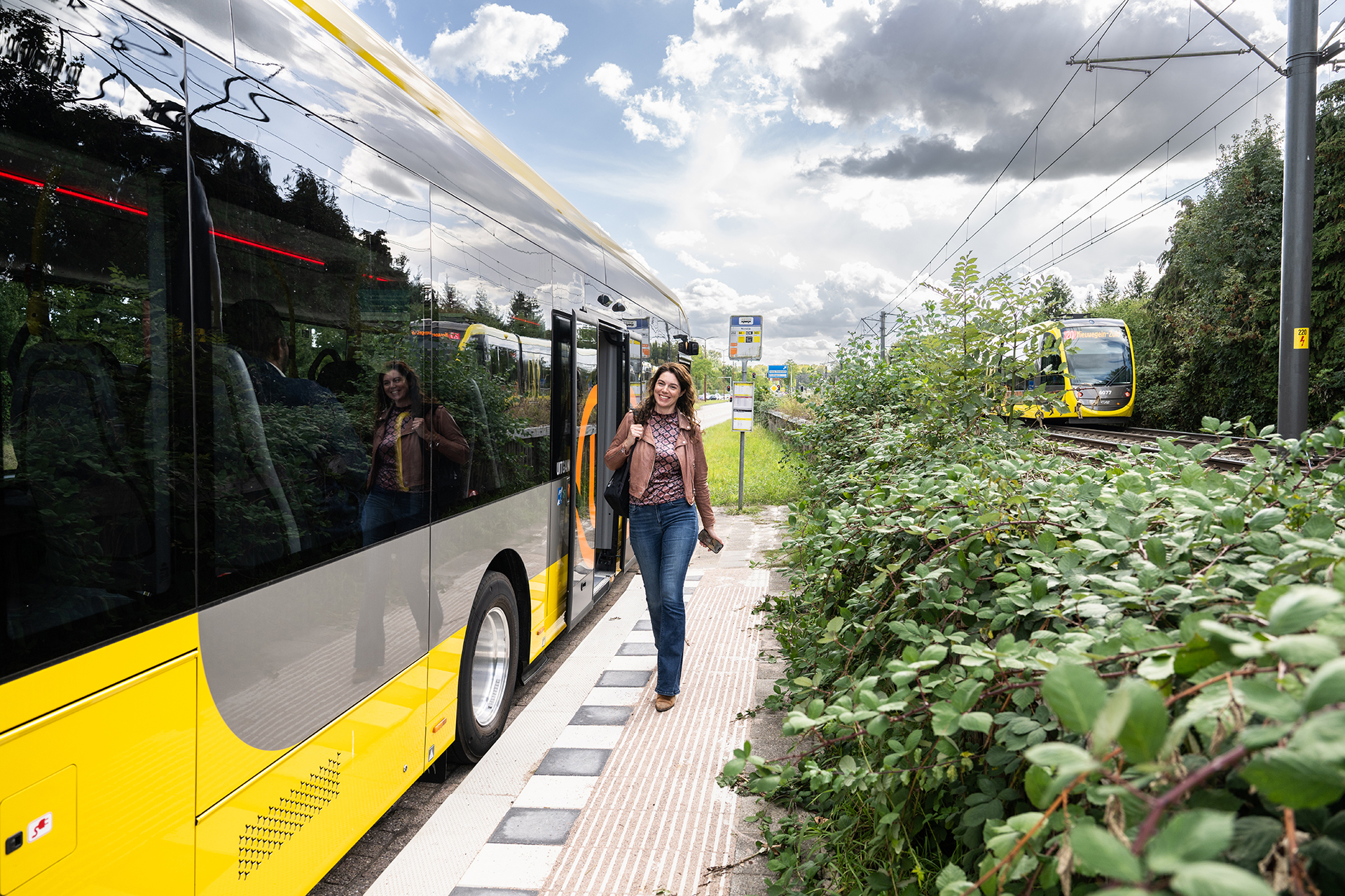 Afbeelding vrouw op bus perron, met tram op de achtergrond