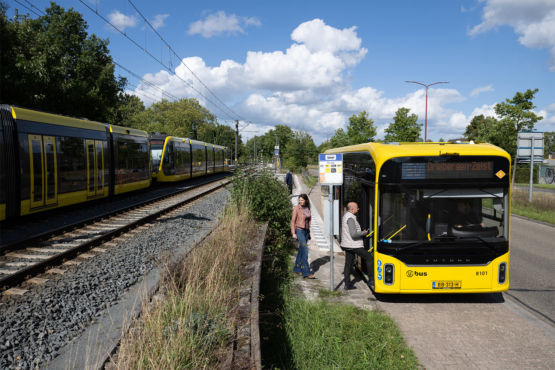 Afbeelding reizigers insappen in bus met daarnaast een langsrijdende tram