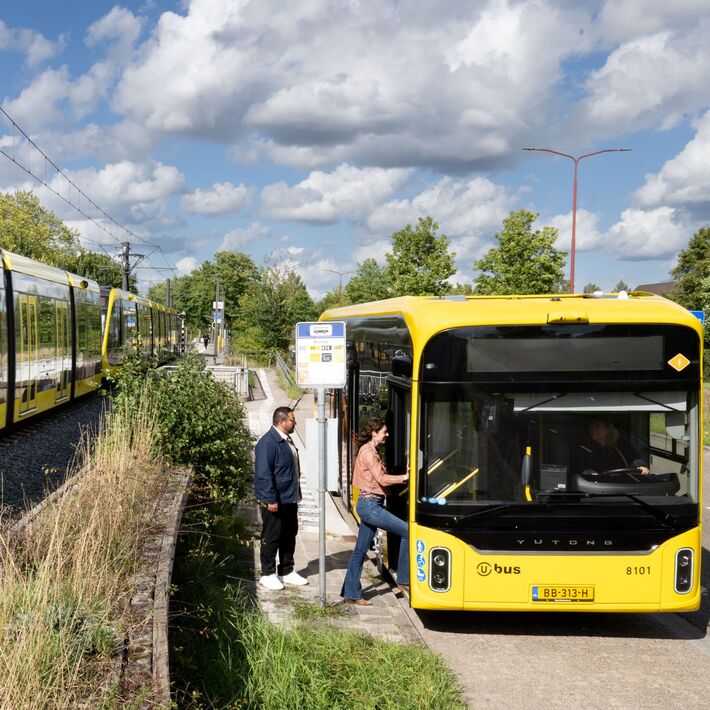 A tram passing a stationary bus where passengers are boarding.