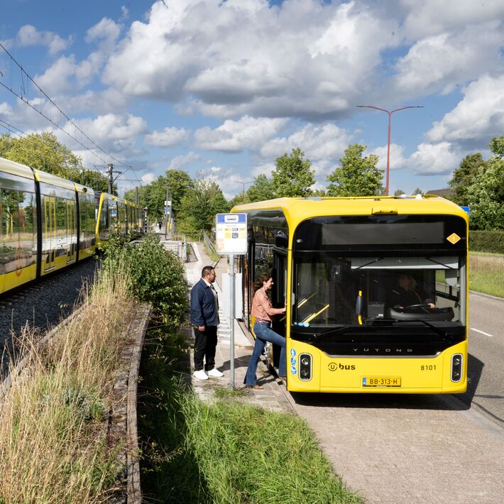 Een tram rijdt langs een stilstaande bus waar passagiers instappen.