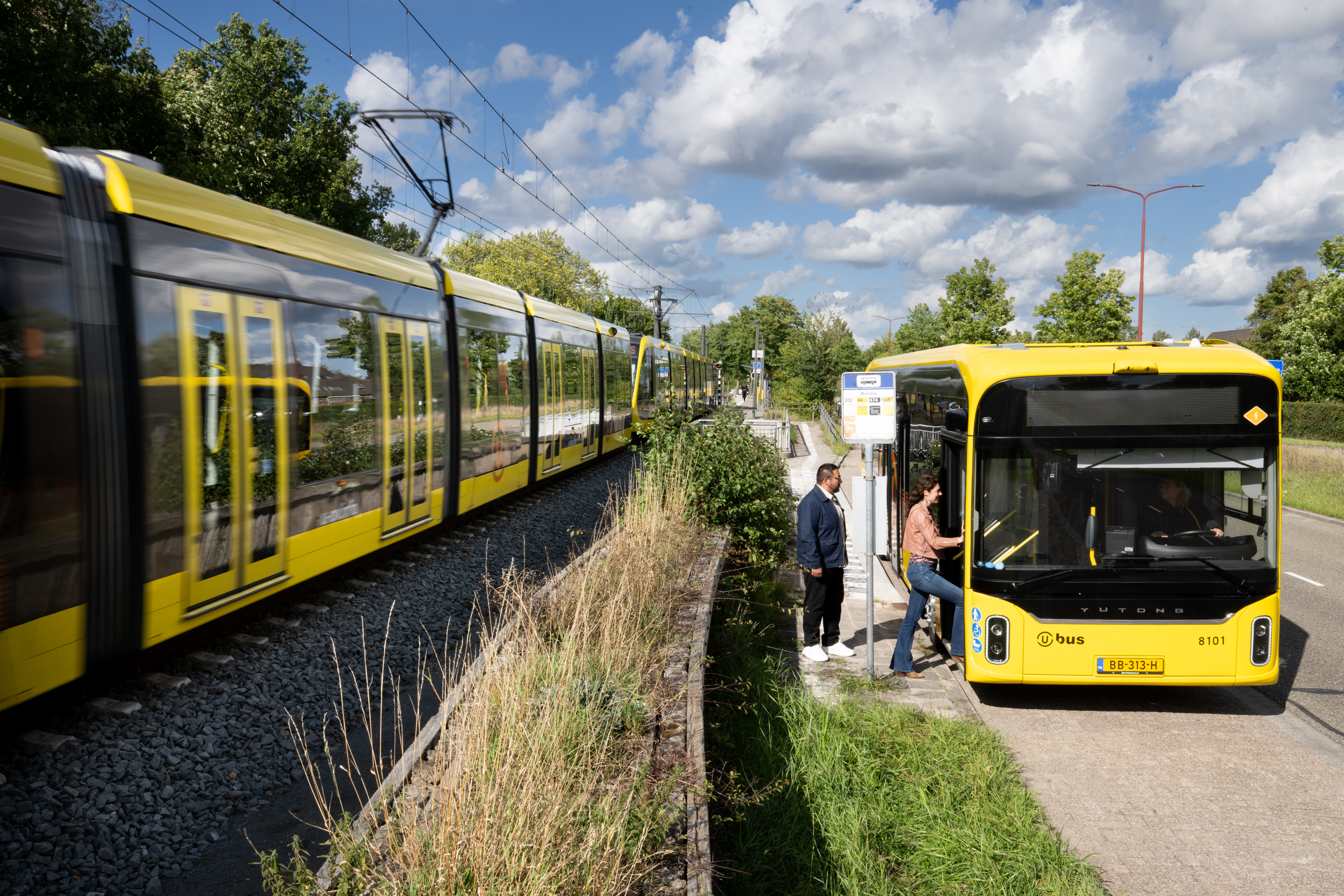 Een tram rijdt langs een stilstaande bus waar passagiers instappen.