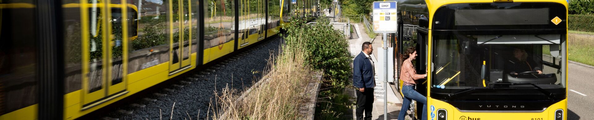 A tram passing a stationary bus where passengers are boarding.