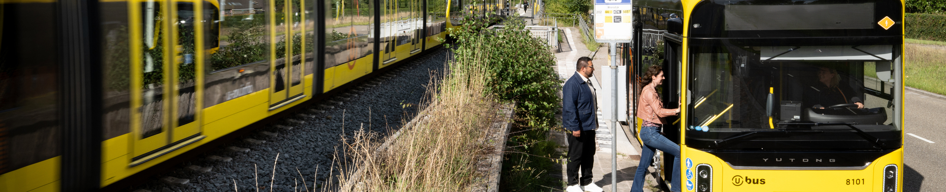 Een tram rijdt langs een stilstaande bus waar passagiers instappen.