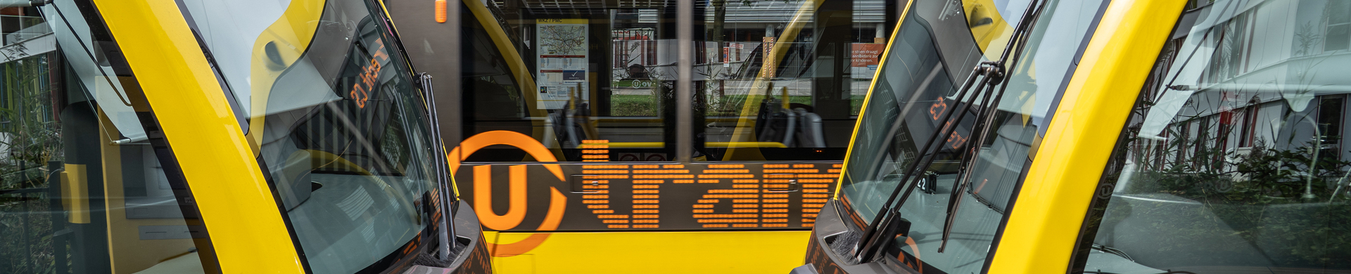 Gele U-tram van U-OV met bestemming Utrecht CS, gefotografeerd tussen twee gekoppelde trams bij een remise in Utrecht.