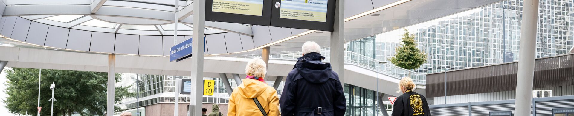 Travellers looking at a digital timetable board at a station.