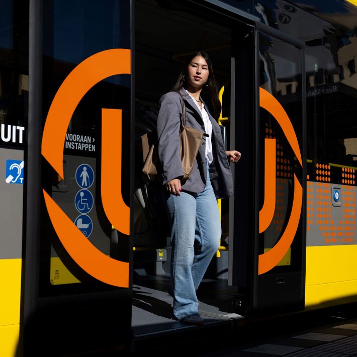 Person steps out of a yellow and gray city bus with orange UOV logo.