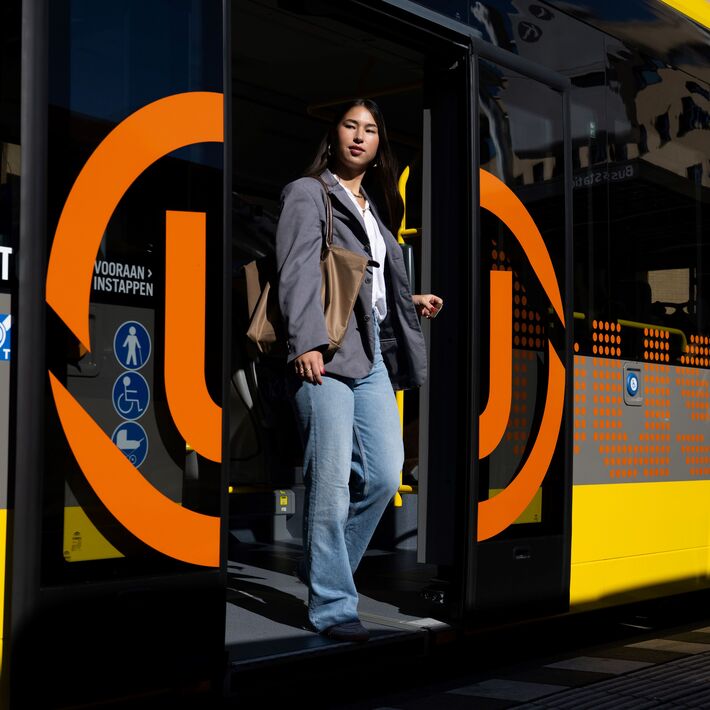 Persoon stapt uit een gele en grijze stadsbus met oranje UOV logo. 