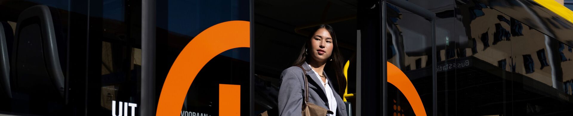 Person steps out of a yellow and gray city bus with orange UOV logo.
