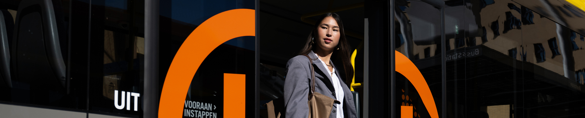 Persoon stapt uit een gele en grijze stadsbus met oranje UOV logo. 