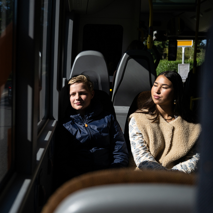 Two young passengers sit on a two-seater in the bus looking outside.