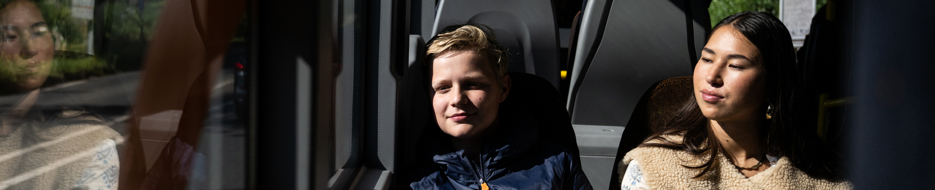 Twee jonge reizigers zitten op een tweezits in de bus en kijken naar buiten.