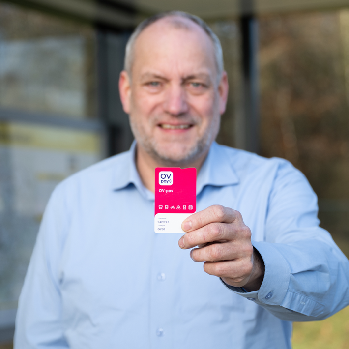 Man at a bus stop holding a public transport pass in his hands.