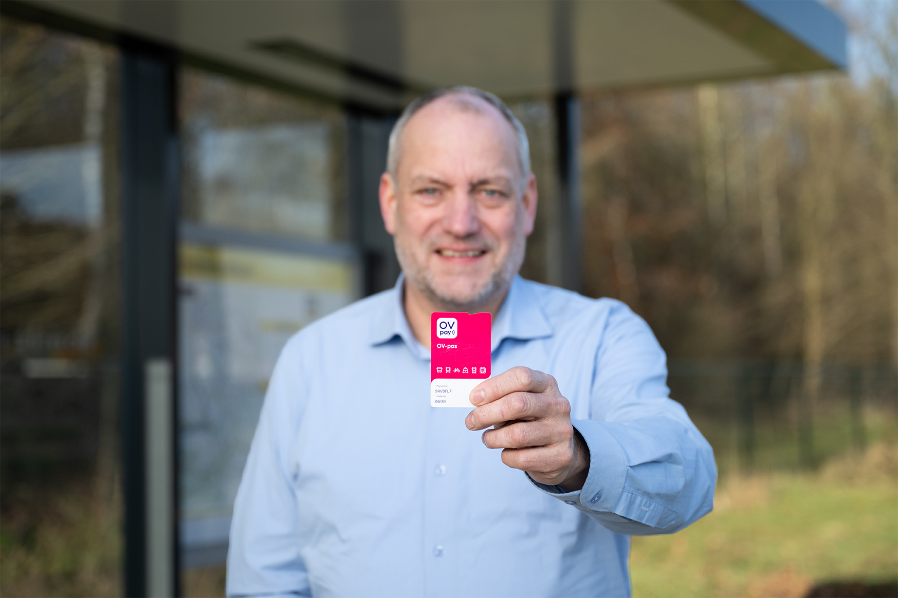Man at a bus stop holding a public transport pass in his hands.