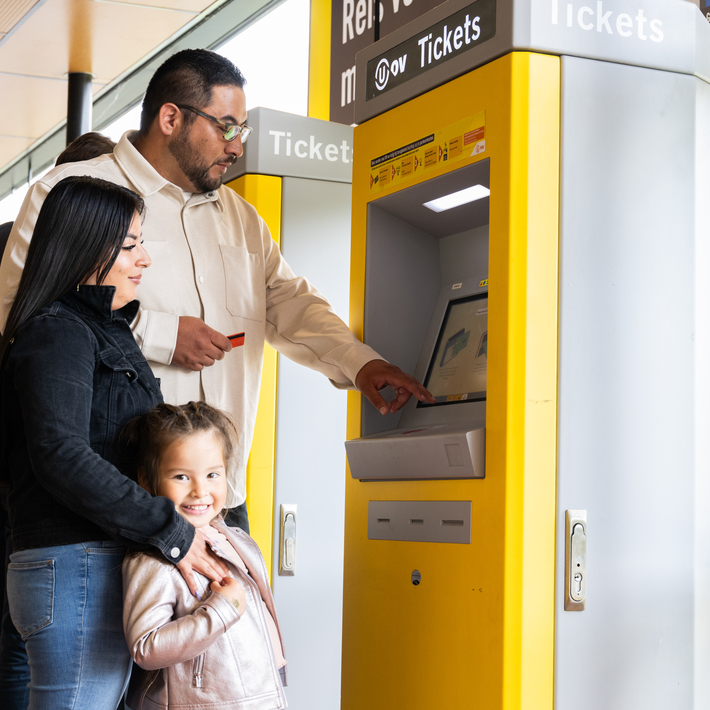 Two adults and one child are at the parking ticket machine paying with a payment card.