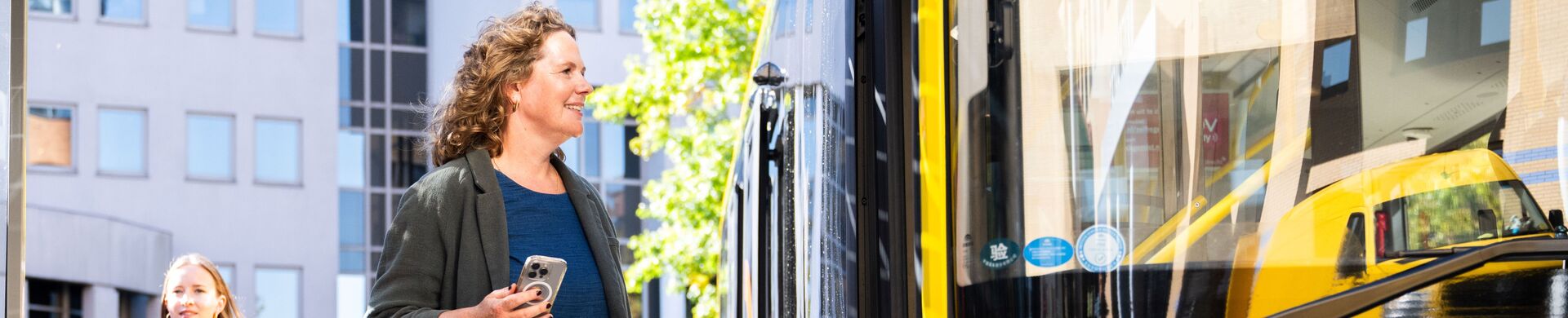 A passenger gets on a yellow bus. Someone walks by.