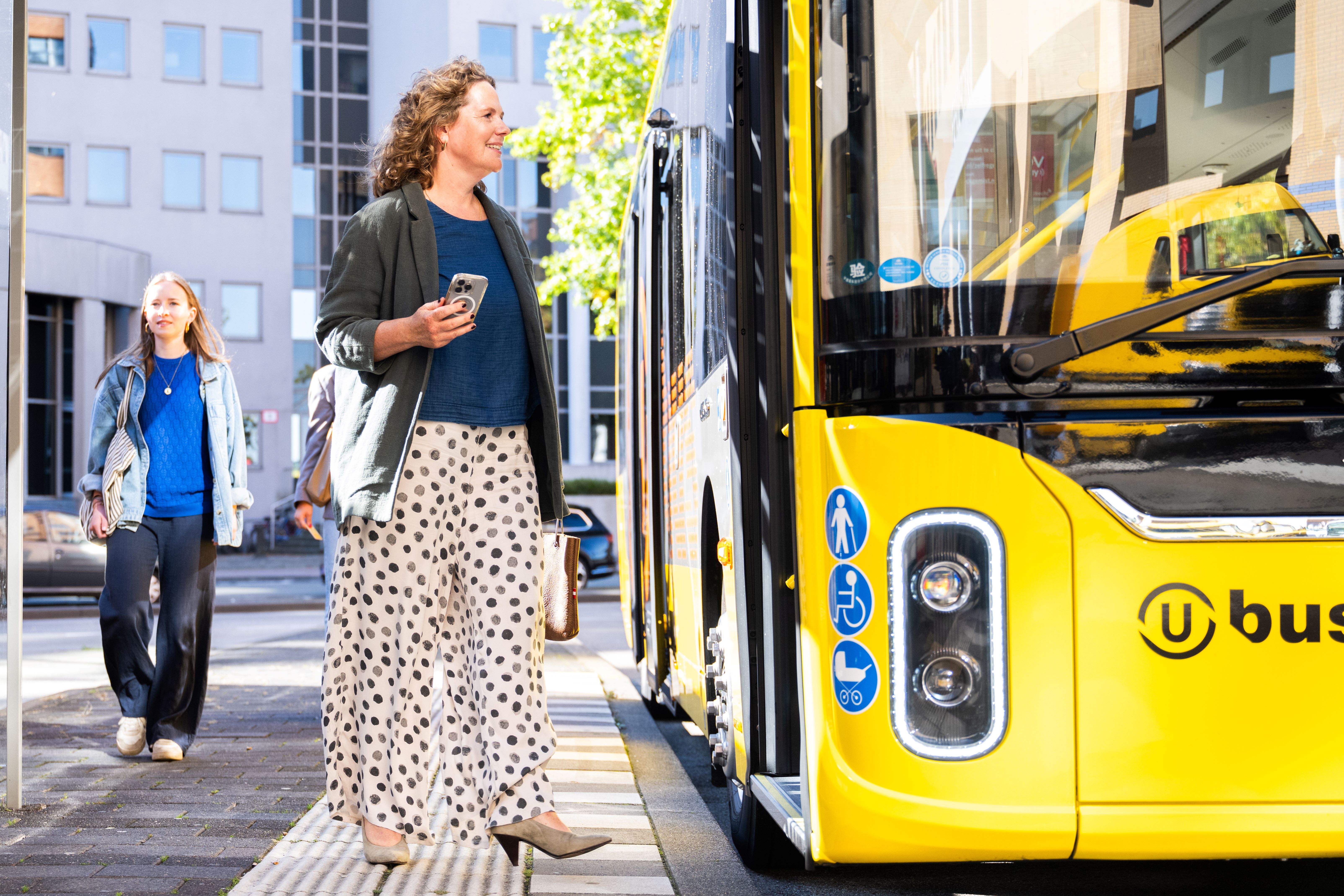 A passenger gets on a yellow bus. Someone walks by.